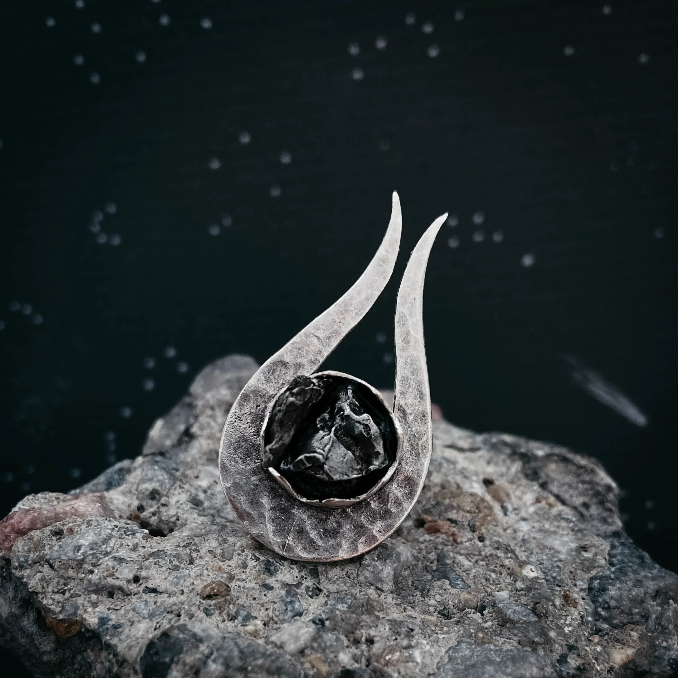 Unique silver pendant with black textured stone on rough gray rock background