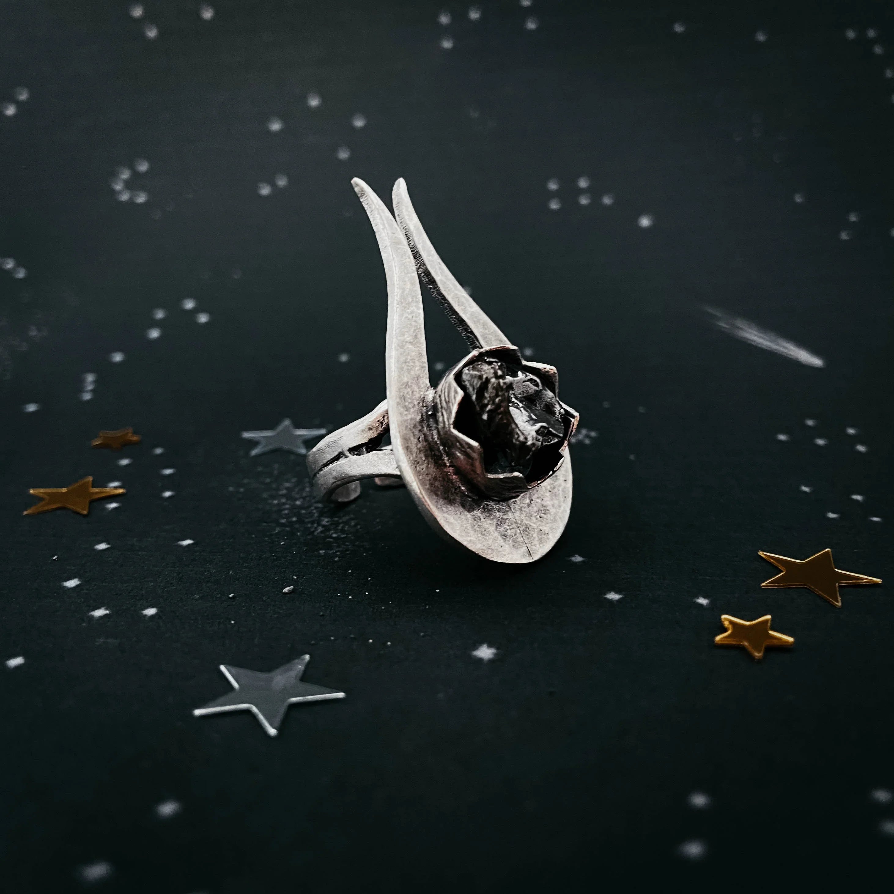 Unique silver ring with abstract design and black stone on starry dark background