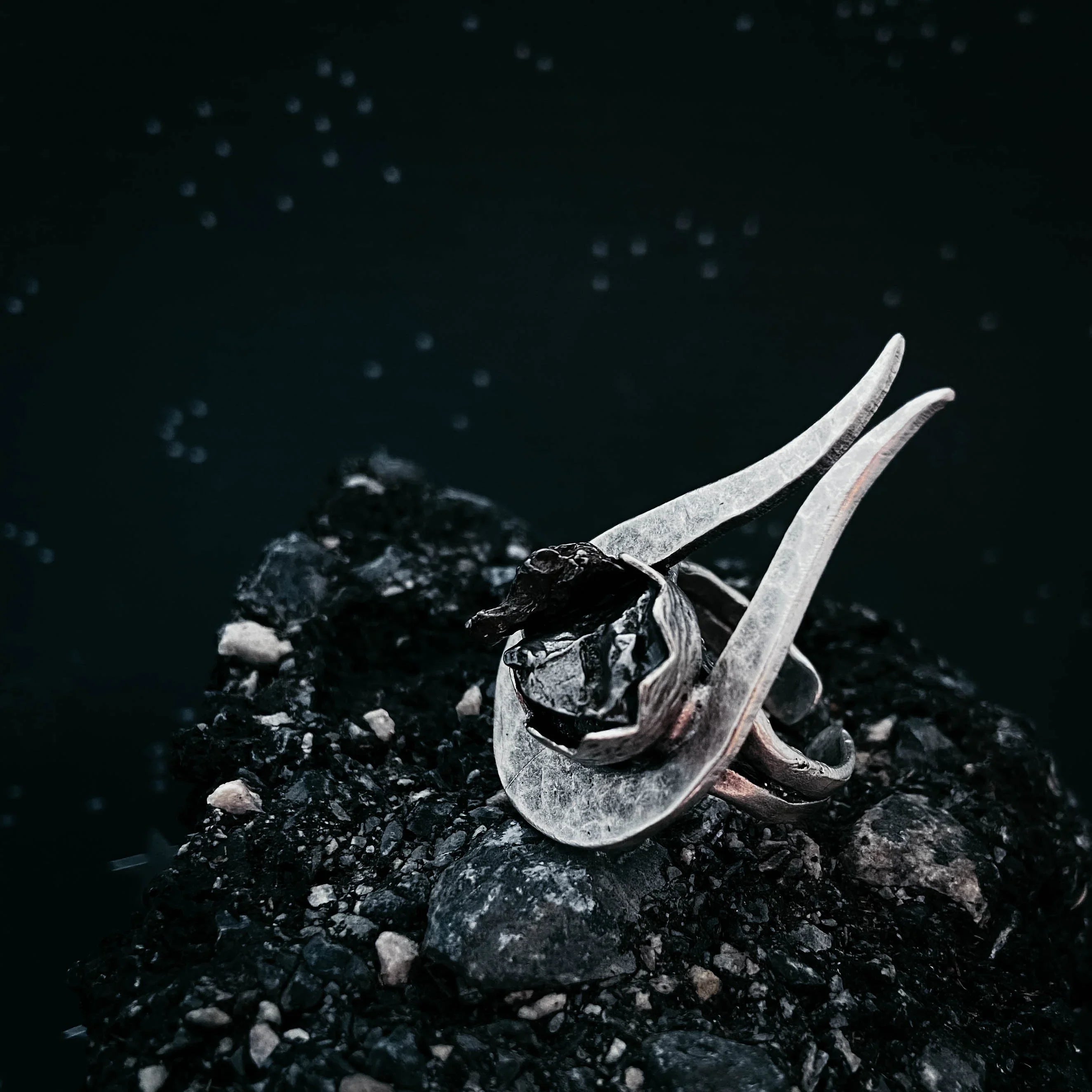 Silver ring with a dark stone centerpiece placed on rough black textured rock surface