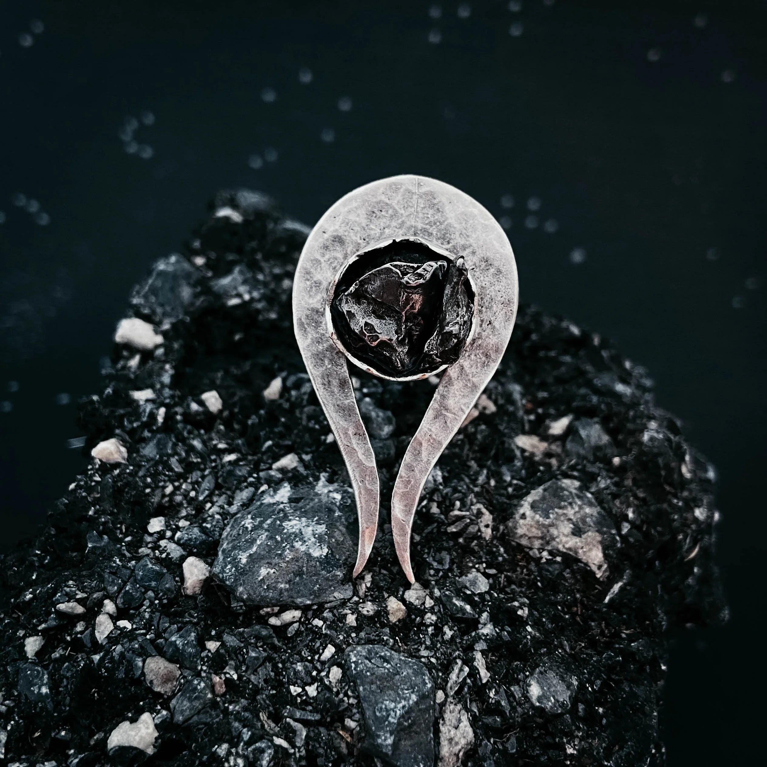Silver ring with a dark stone displayed on rough black gravel background