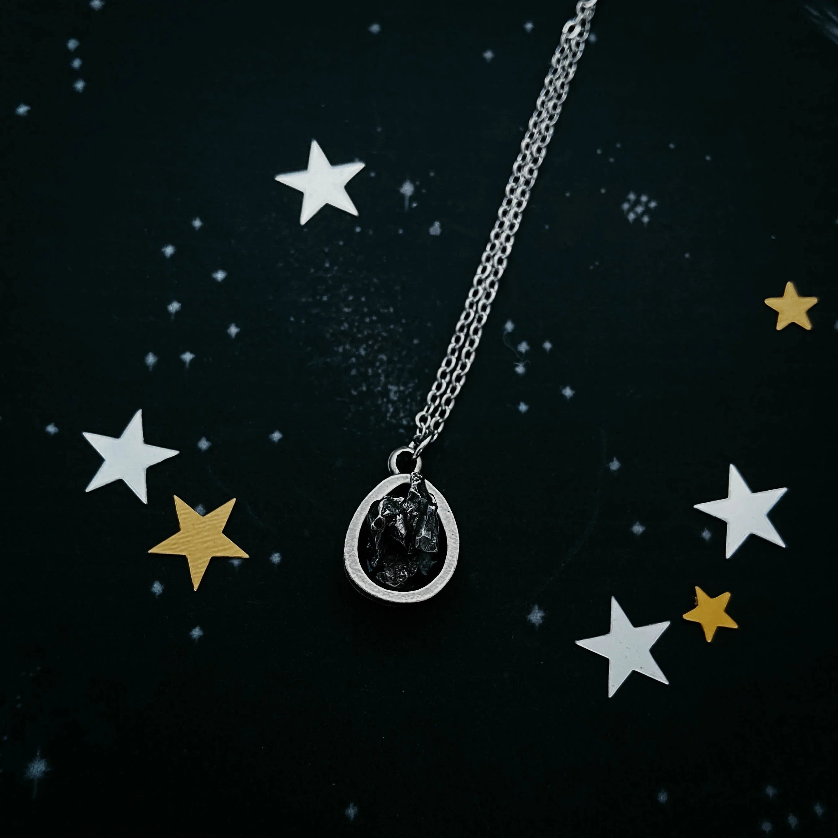 Cosmic-inspired silver pendant necklace with raw black stone, surrounded by star confetti