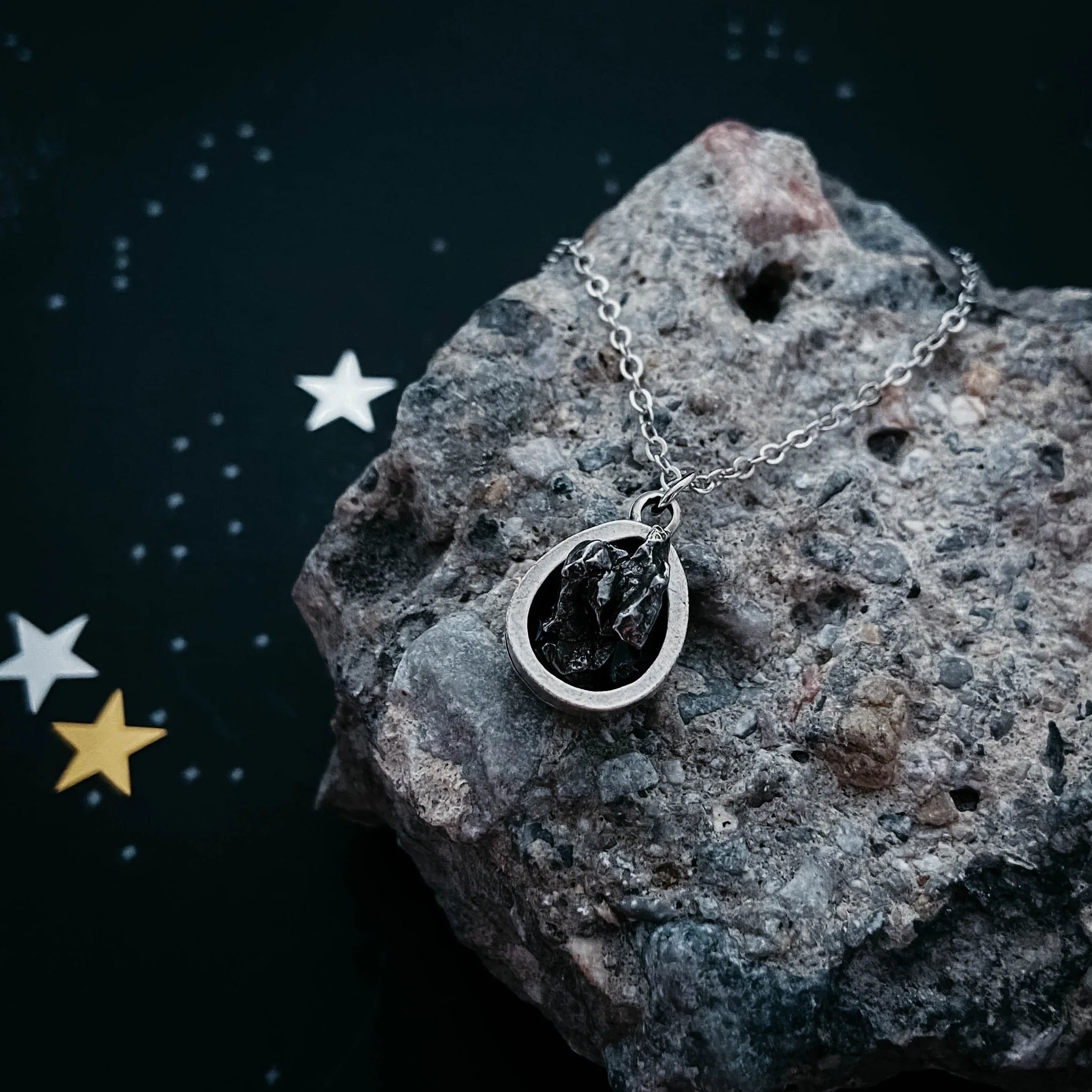 Cosmic-inspired silver pendant necklace with black stone on rock, Qu!rk Boutique gift background