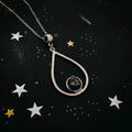 silver teardrop pendant necklace featuring a black raw stone on a starry black background