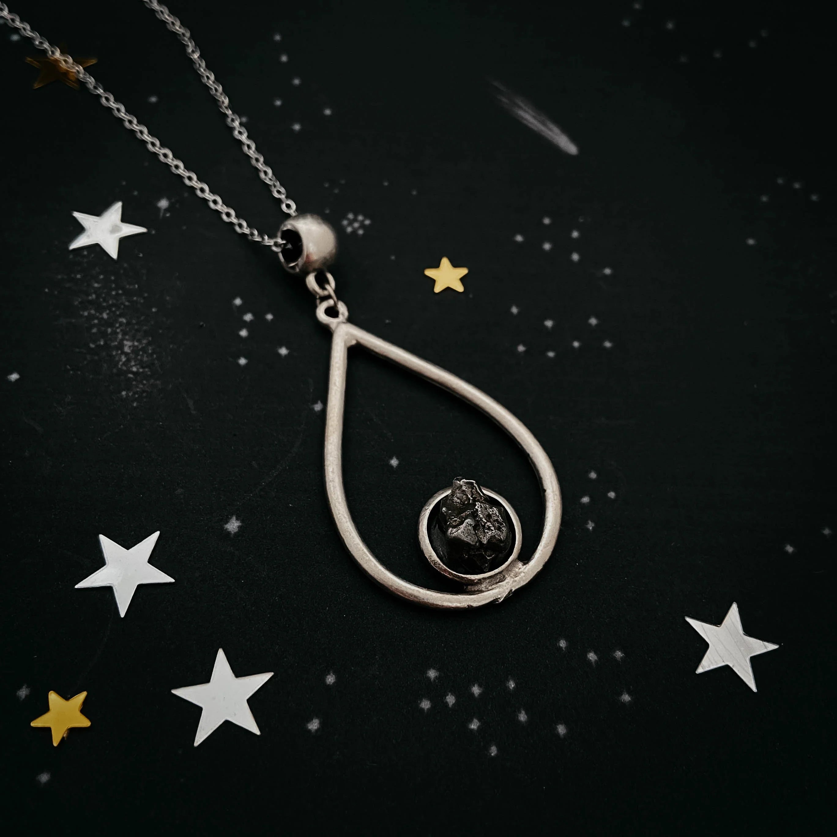 silver teardrop pendant necklace featuring a black raw stone on a starry black background