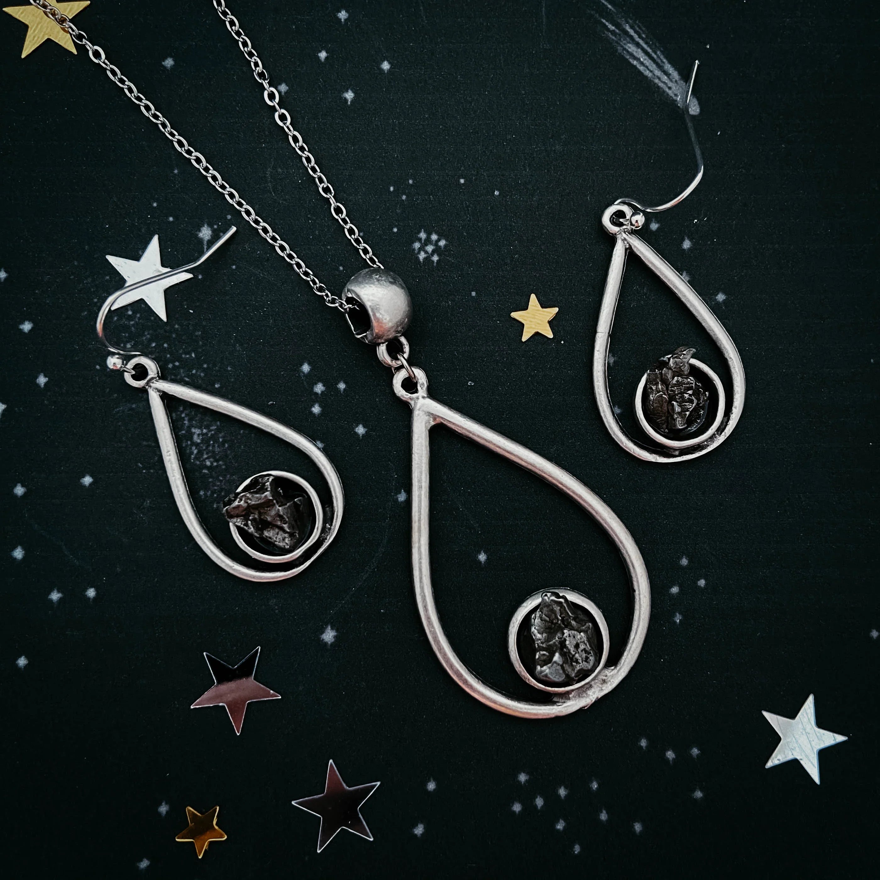 Silver teardrop pendant necklace and matching earrings with black stones on starry background