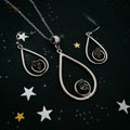Silver teardrop jewelry set with black stone center on dark background with star decorations