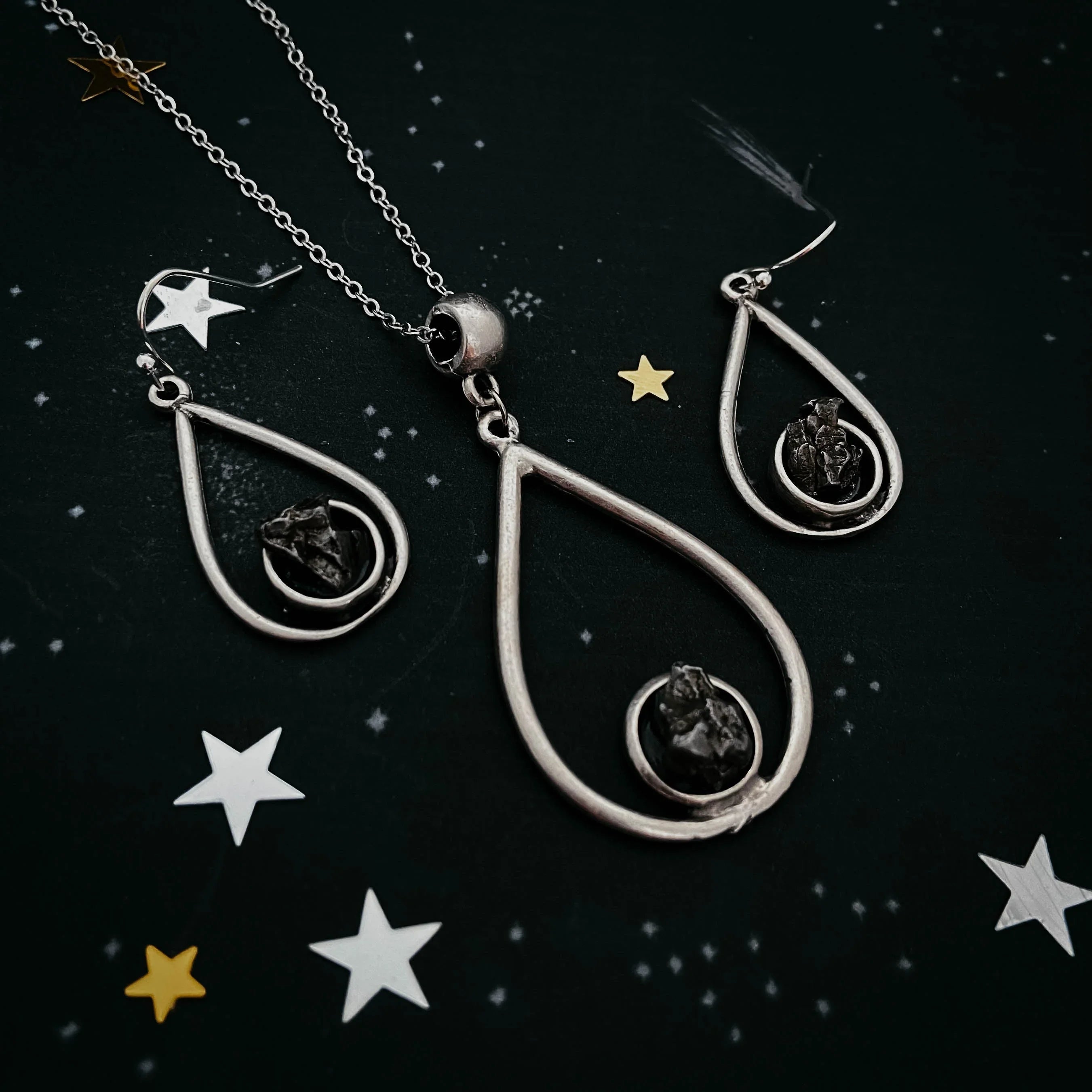 Silver teardrop jewelry set with black stone center on dark background with star decorations