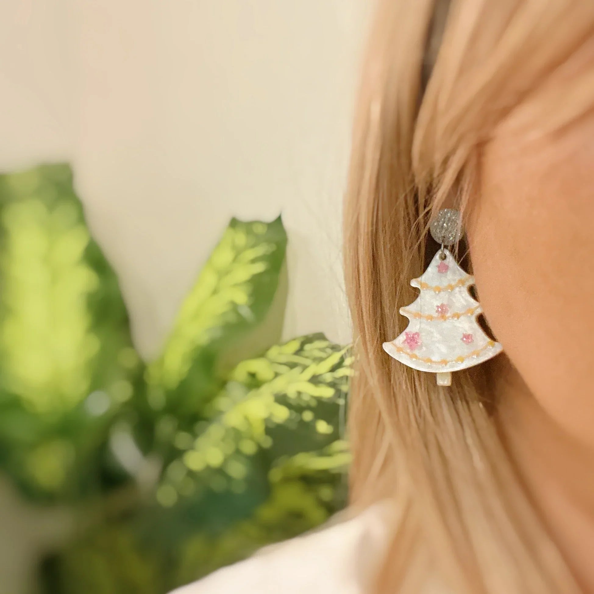 Close-up of a white Christmas tree-shaped earring with pink decorations on a woman's ear