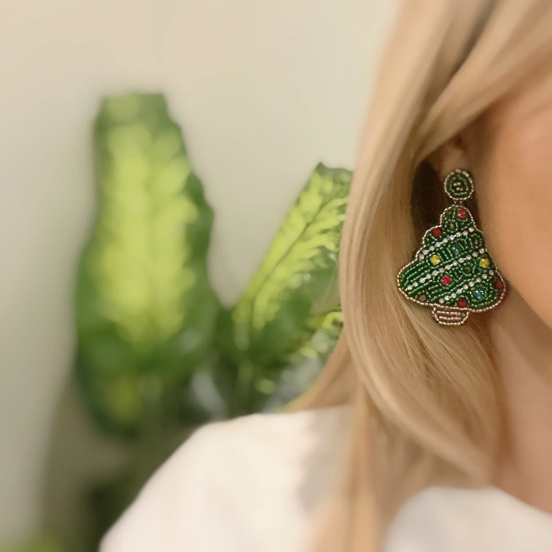 Close-up of woman wearing beaded green Christmas tree earrings with colorful details