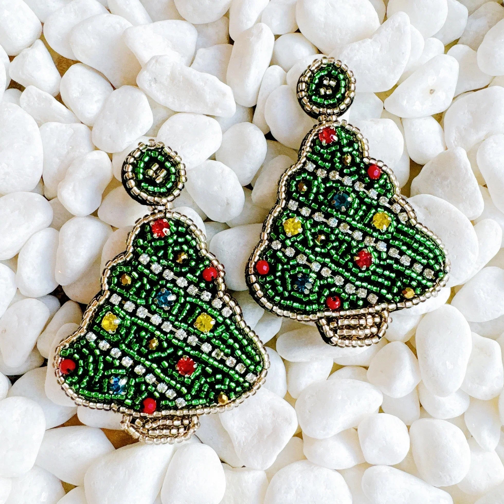 Pair of Christmas tree shaped earrings with green beads and colorful decorations on white pebbles