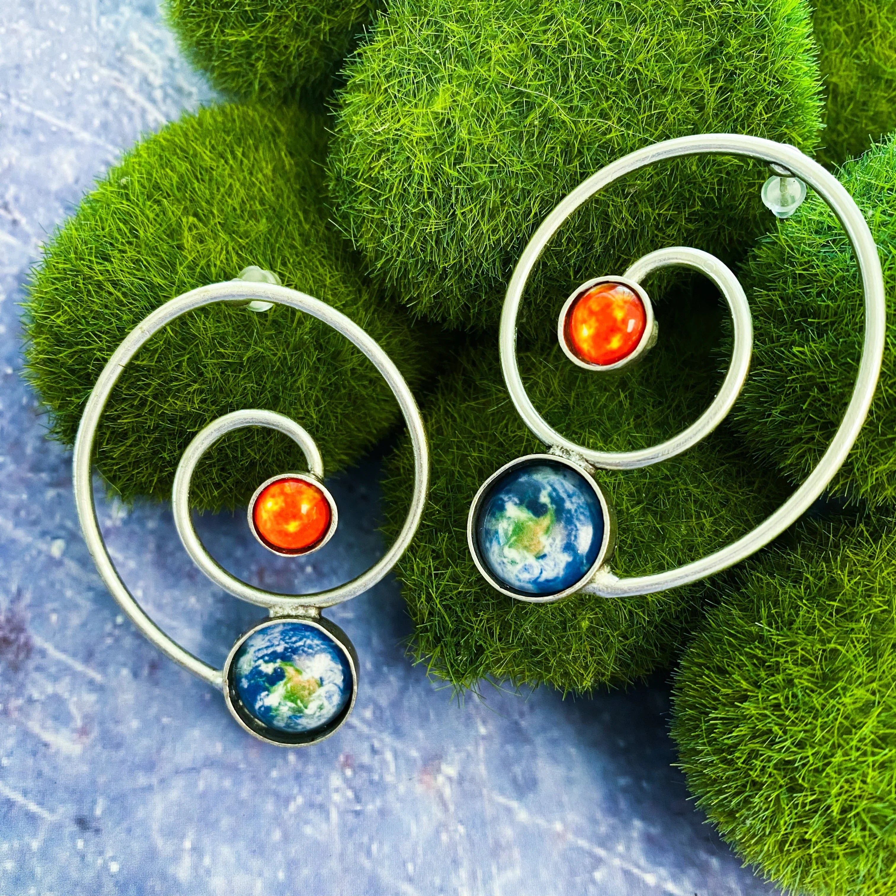 Artist-designed cosmic spiral earrings with Earth and sun motifs on green moss, Qu!rk Boutique