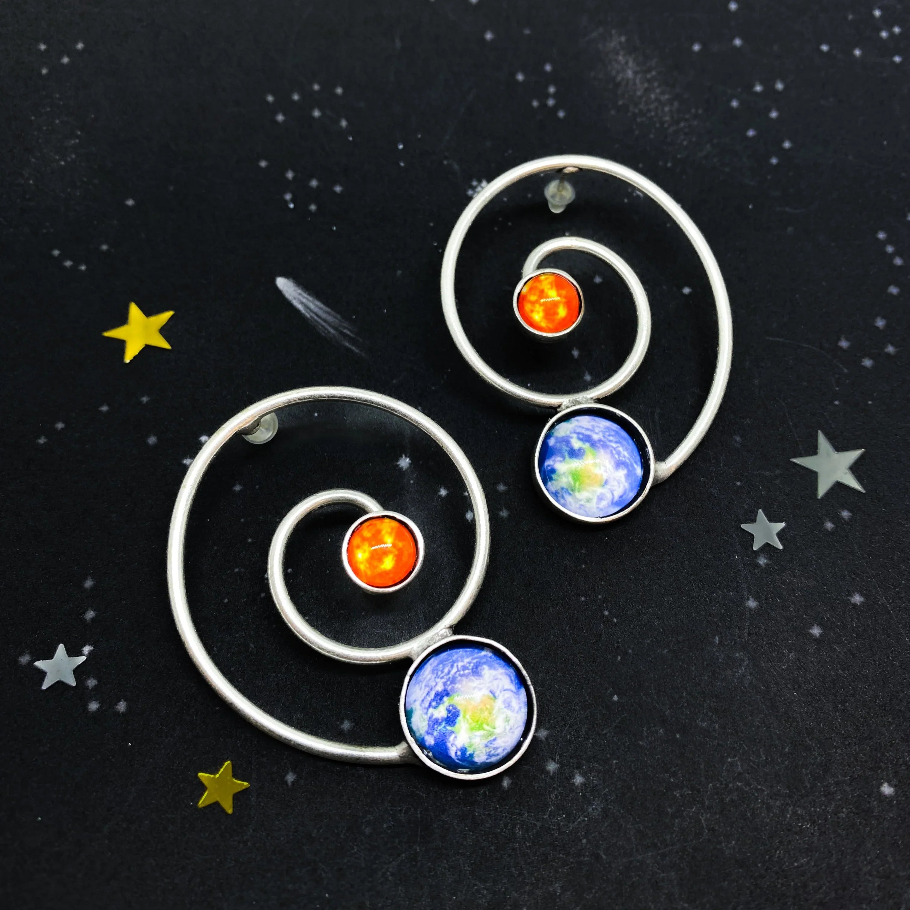 Cosmic spiral earrings with sun and earth design on starry background at Qu!rk Boutique