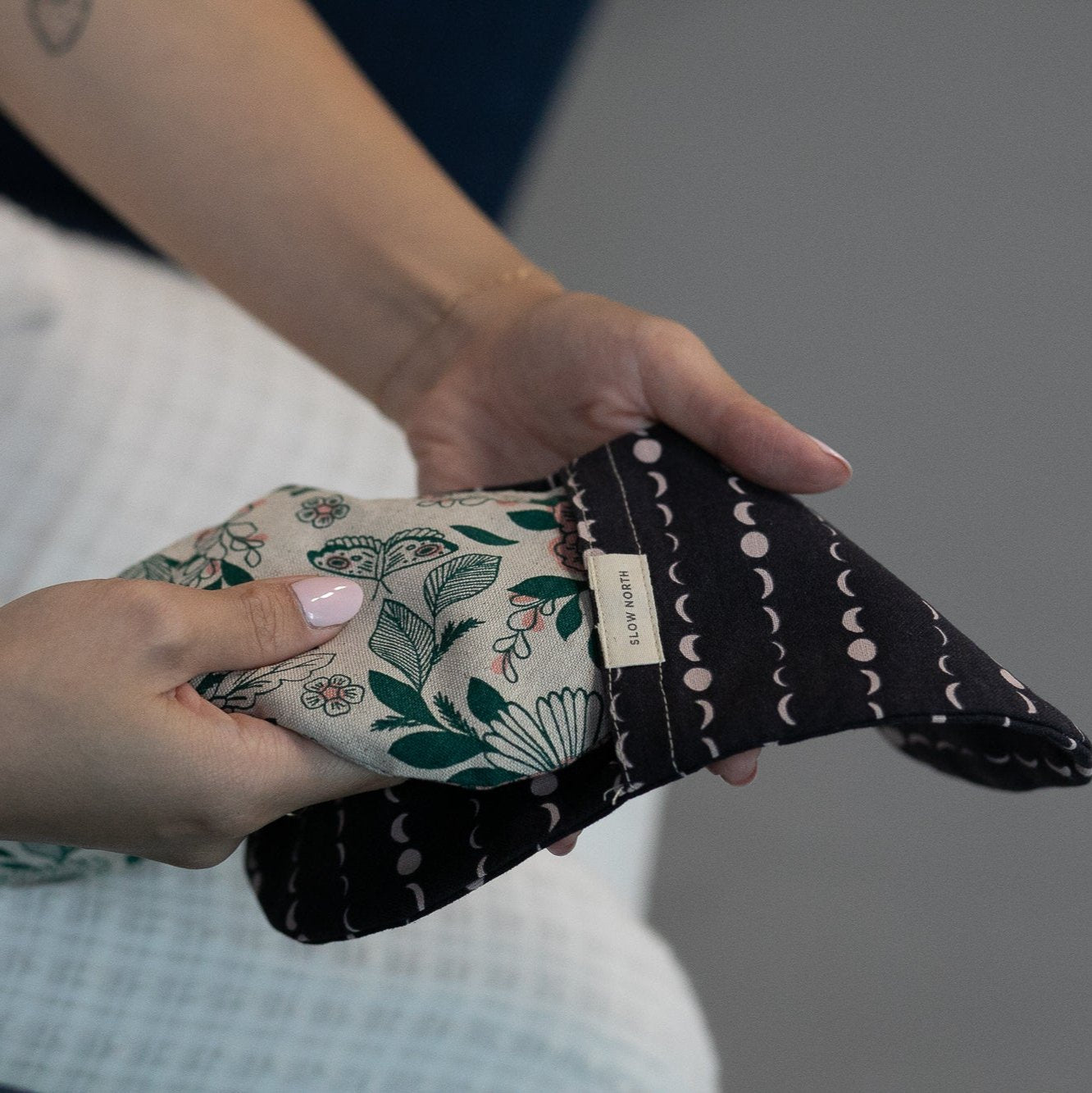 Hands holding a floral and moon phase patterned fabric pouch with Slow North label