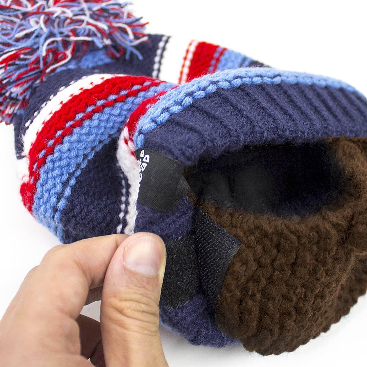 Hand holding a navy blue, red, white, and light blue knit winter hat with a pom-pom and brown fleece lining