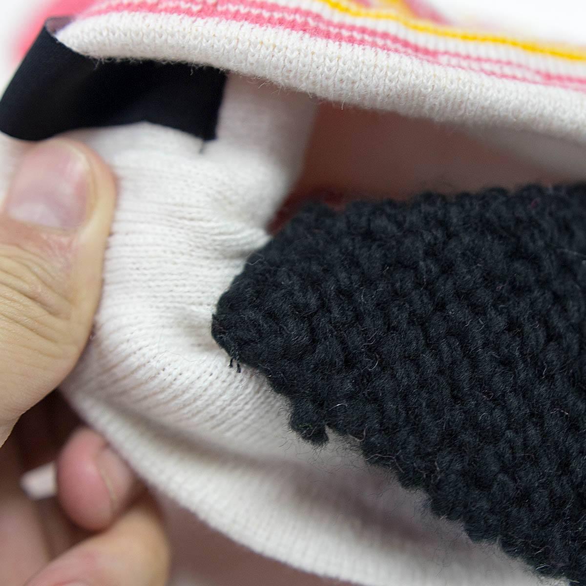 Close-up of hand holding folded white knit fabric with multicolor stripe and textured black patch