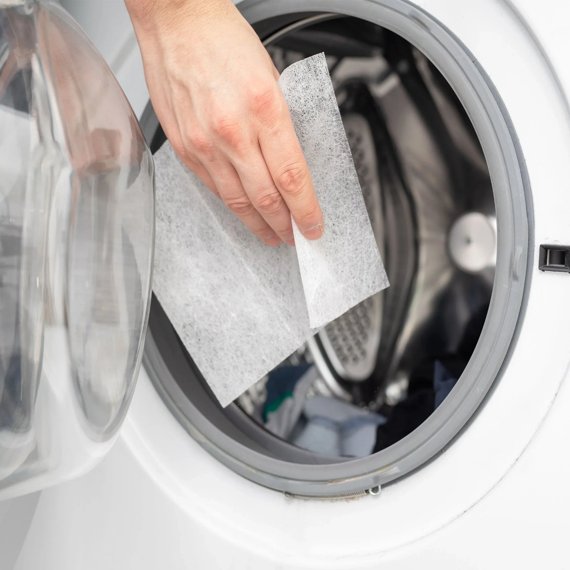 Hand placing eco-friendly dryer sheet into front-load washing machine, Qu!rk Boutique
