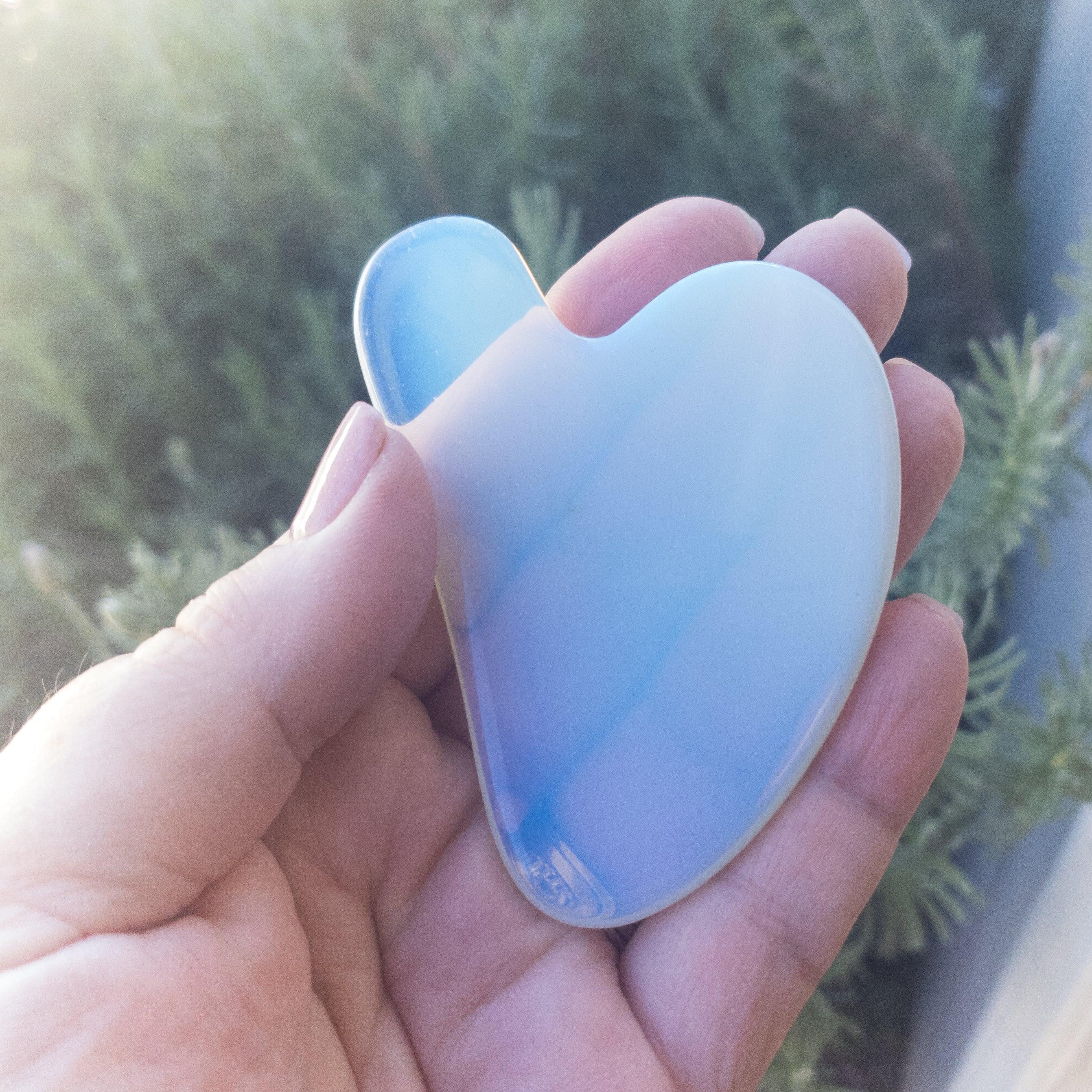 Hand holding a pastel opalite heart-shaped gua sha tool outside, Qu!rk Boutique artisan gift