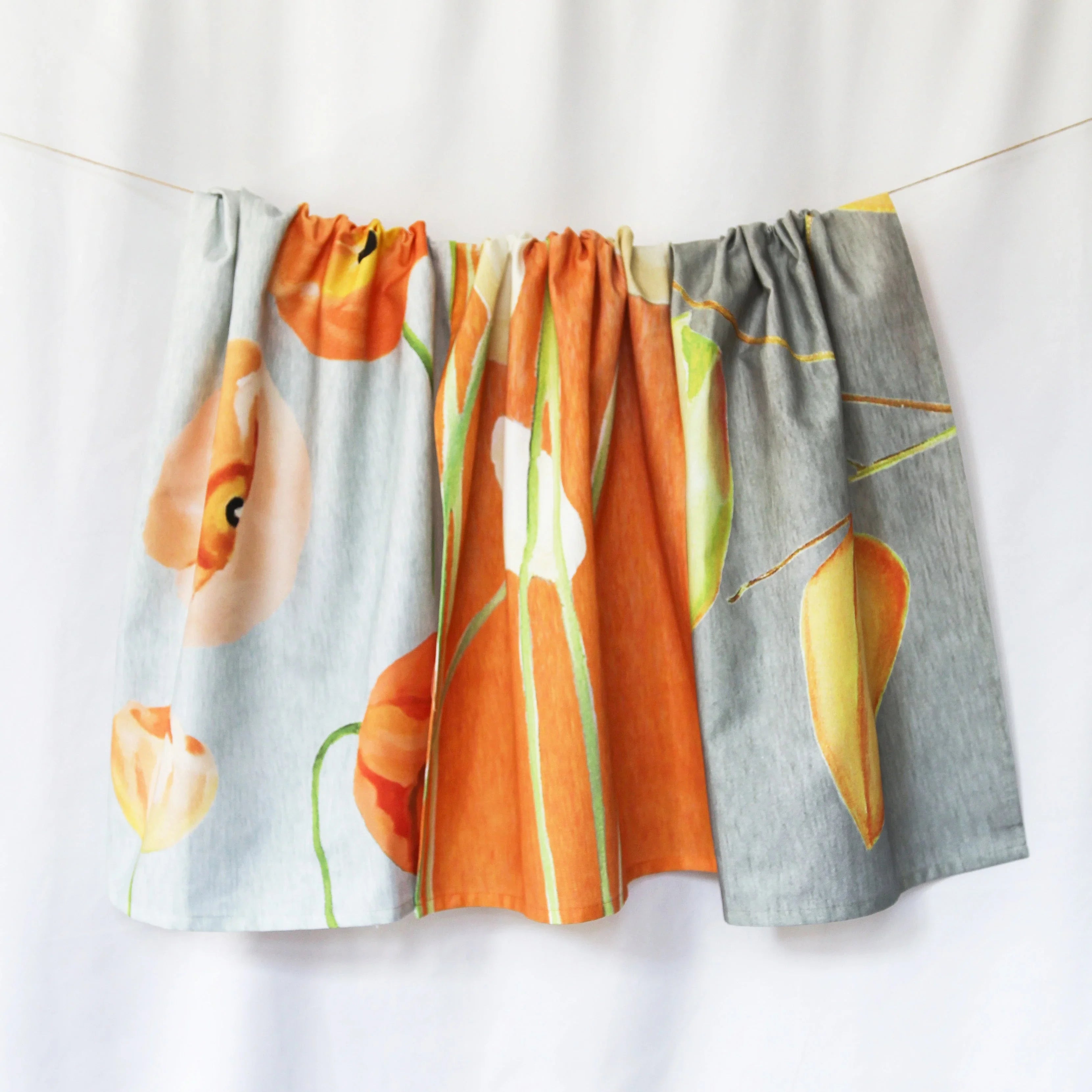 Artist-designed tea towel with bold orange and yellow poppy floral print, displayed on a line.