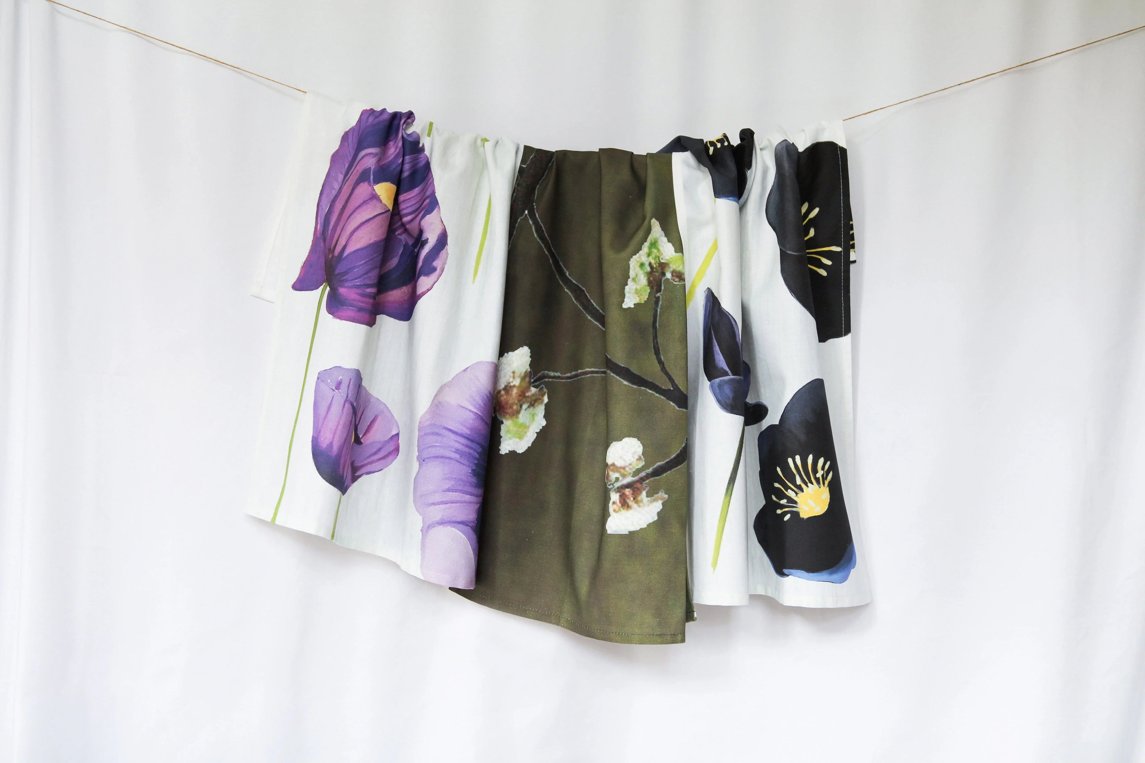 Floral tea towels with purple, white, and black flower prints hanging on a white background
