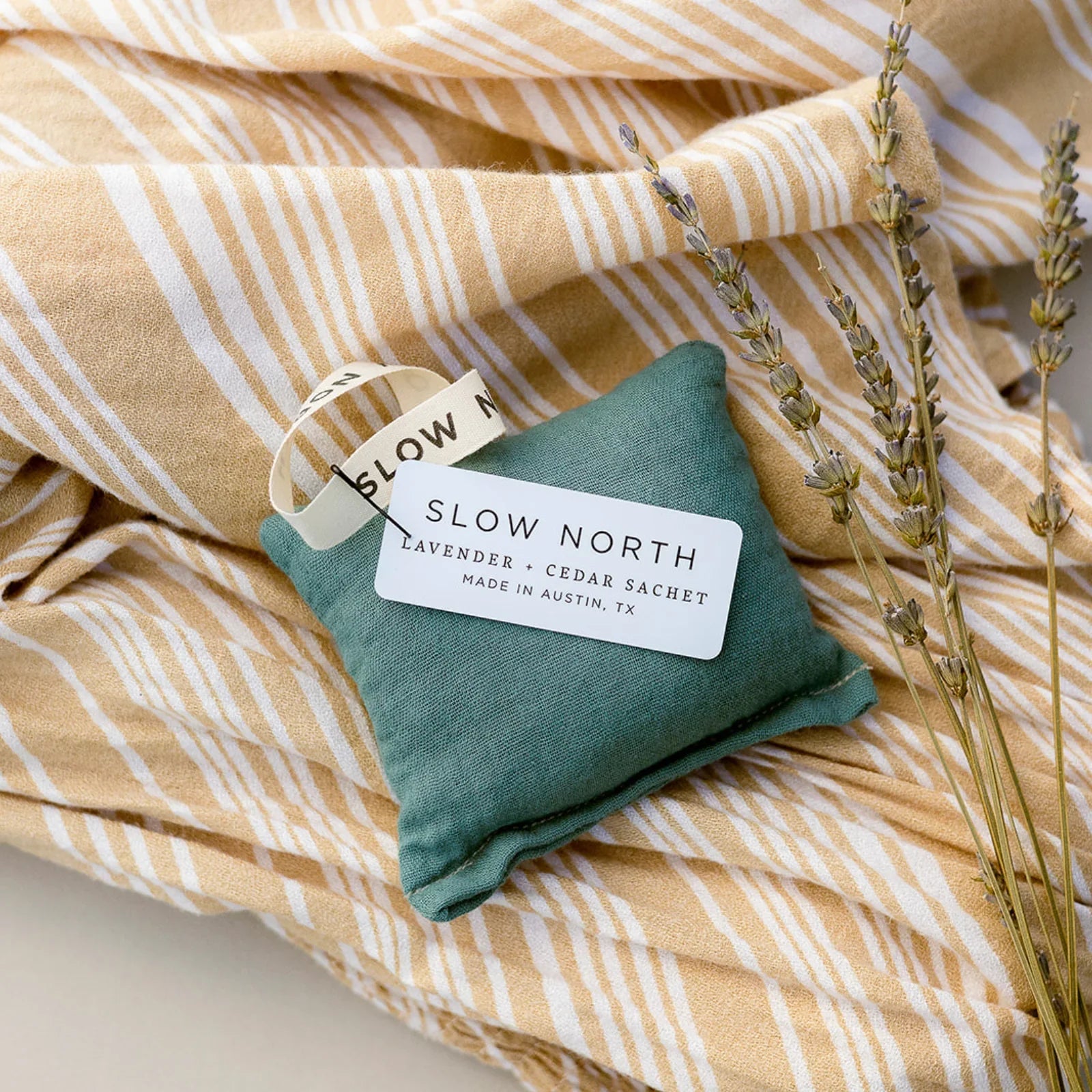 Slow North lavender and cedar sachet with tag on green pouch, beige striped fabric and dried lavender sprigs