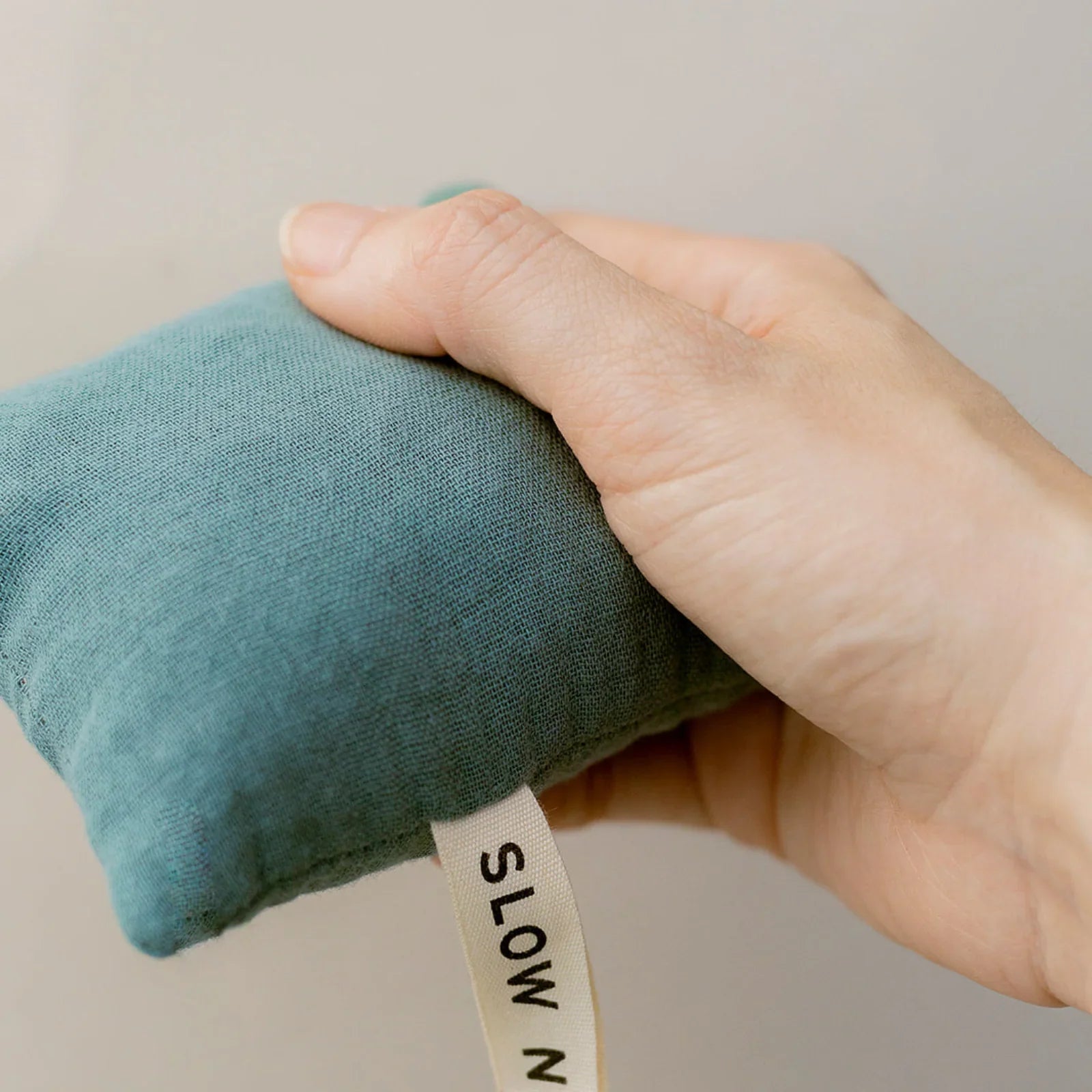 Hand holding small blue-green fabric pouch with 'SLOW N' label tag