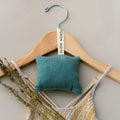 Wooden hanger with a yellow patterned dress, blue hanging sachet labeled Slow North, and dried lavender sprigs
