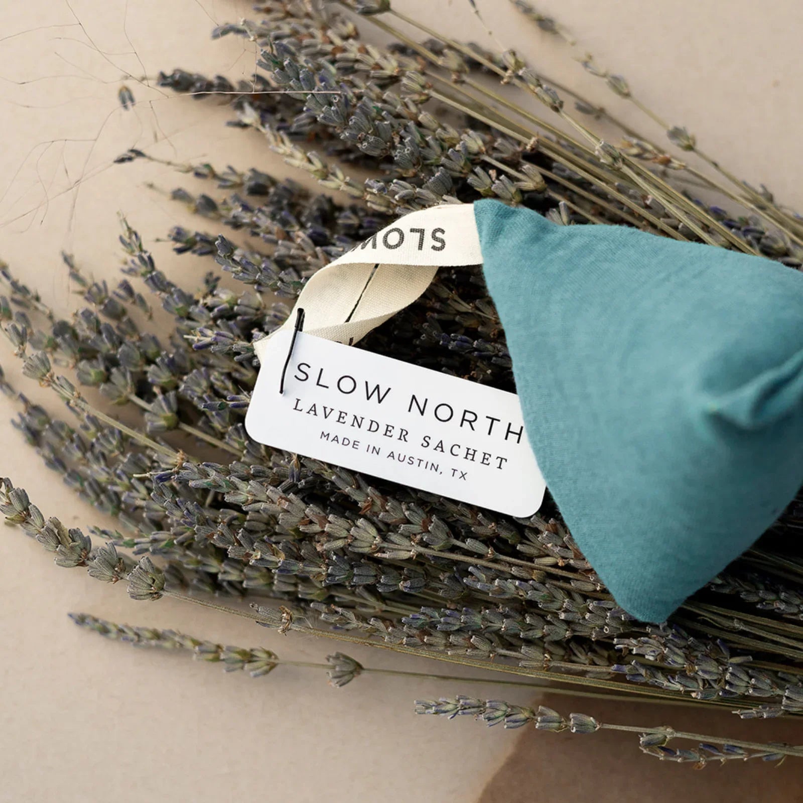Blue fabric lavender sachet with Slow North tag resting on dried lavender bundle