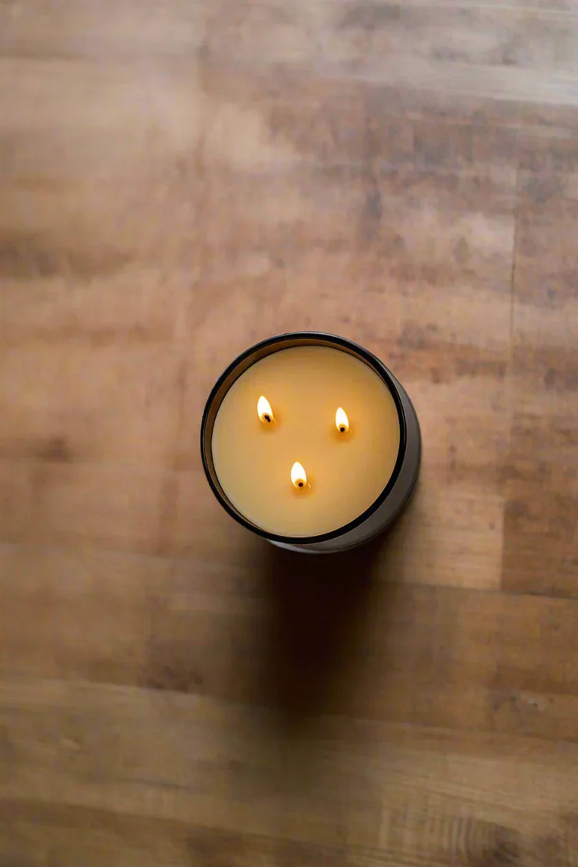 Top view of a large three-wick natural candle burning on a wooden surface