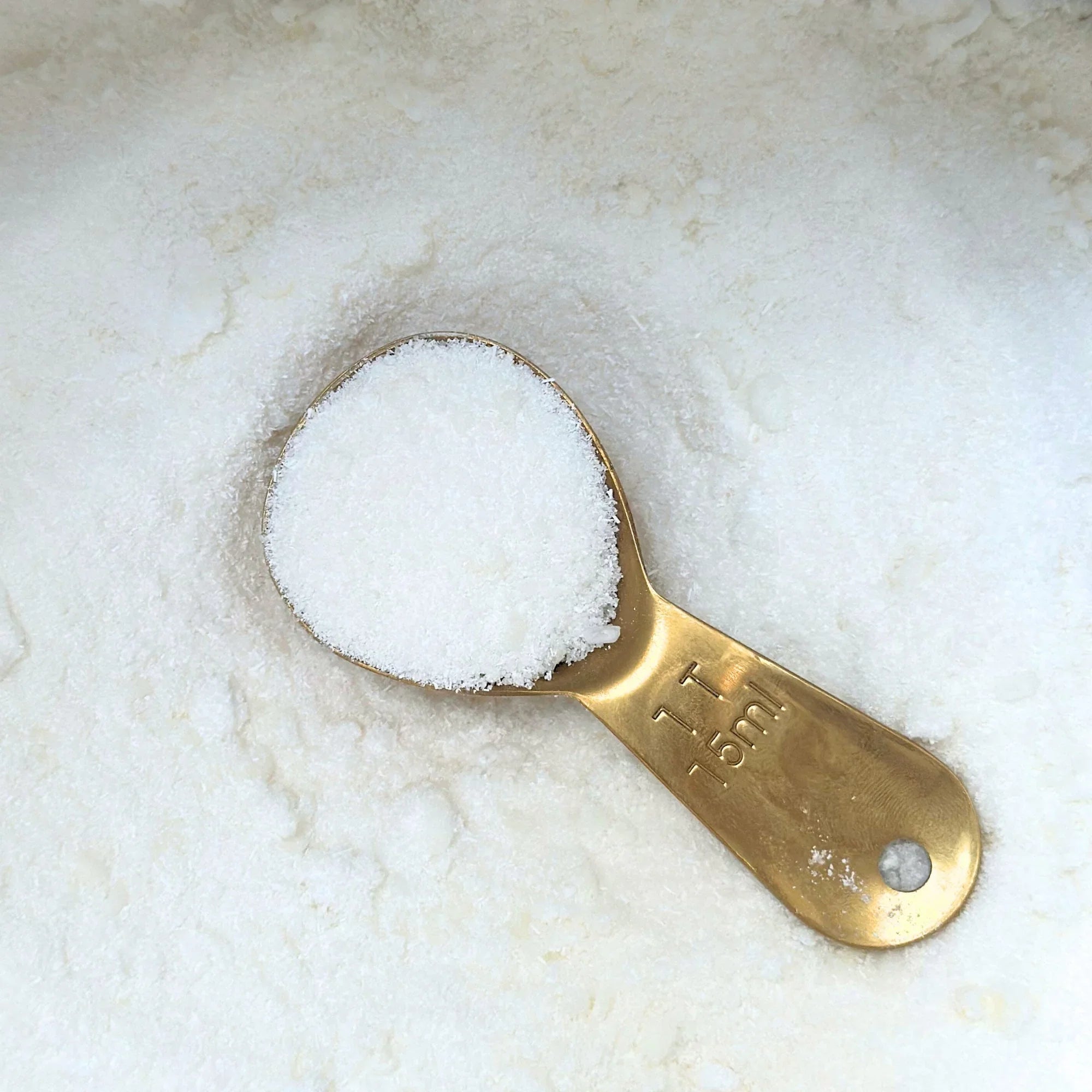 Brass measuring spoon with 1 tablespoon of fine white laundry powder on a heap of powder