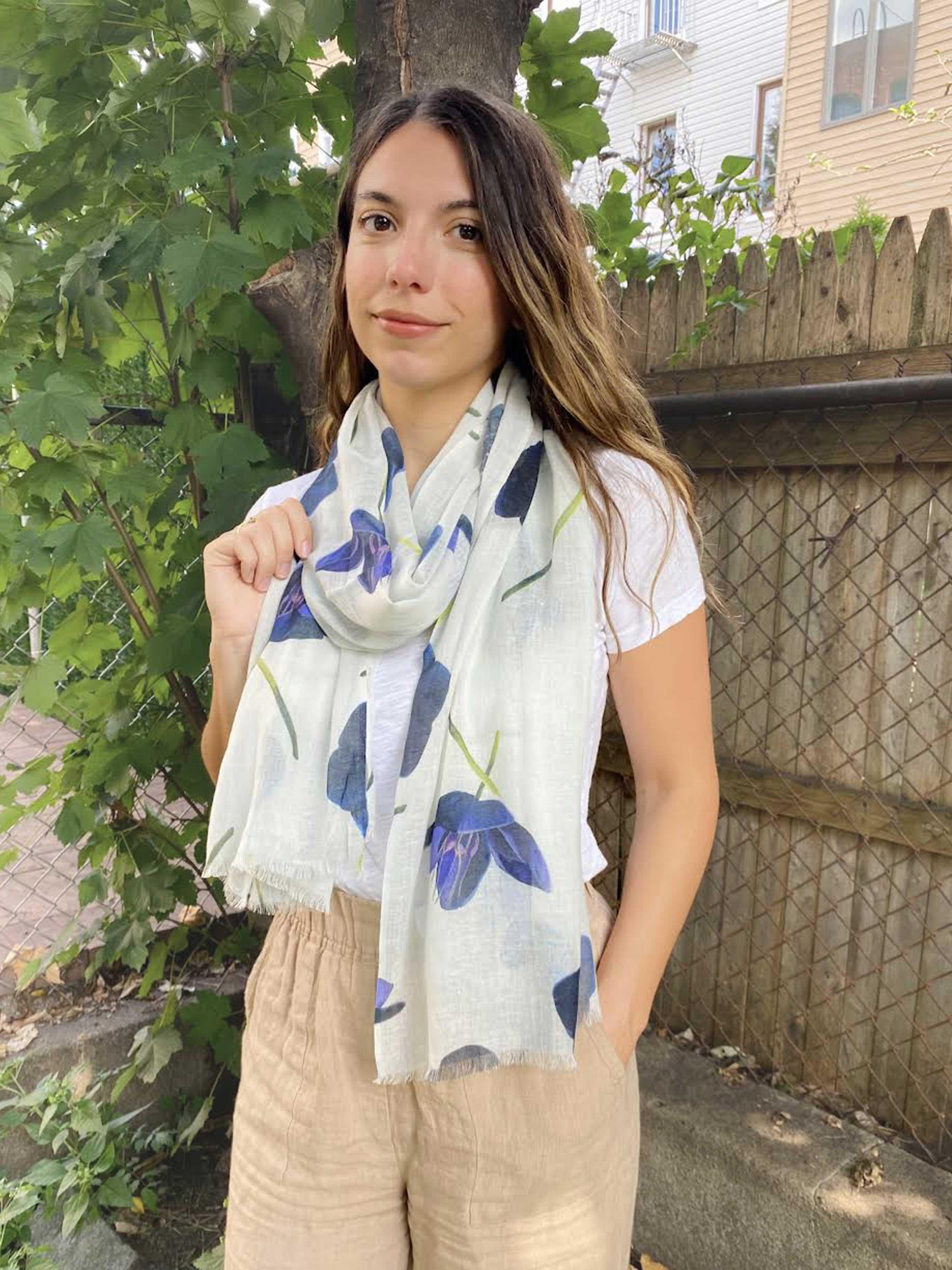 Woman wearing white floral scarf with blue hellebore flowers and beige pants outdoors