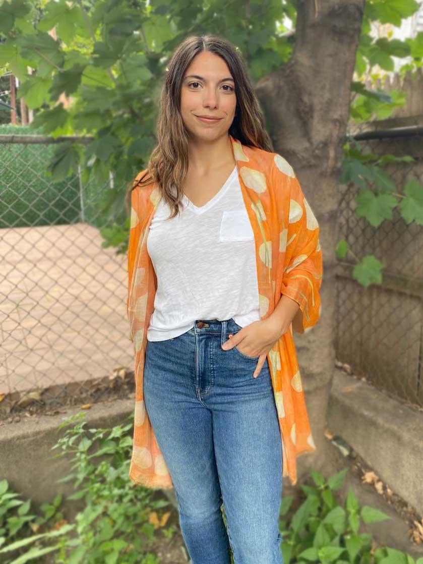 Woman wearing an orange scarf with cream polka dots, white t-shirt, and blue jeans outdoors