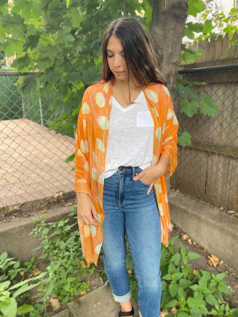 Woman wearing an orange floral scarf over a white shirt and blue jeans in a green backyard