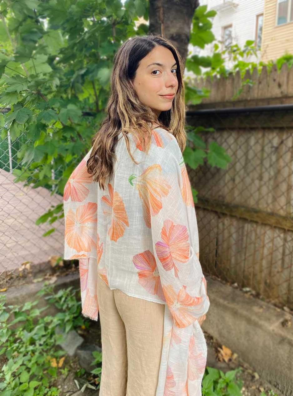 Woman outdoors wearing a white scarf with large orange hibiscus floral print and beige pants