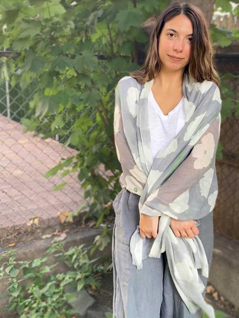 Young woman outdoors wearing a white top and gray floral poppies scarf wrapped around her shoulders