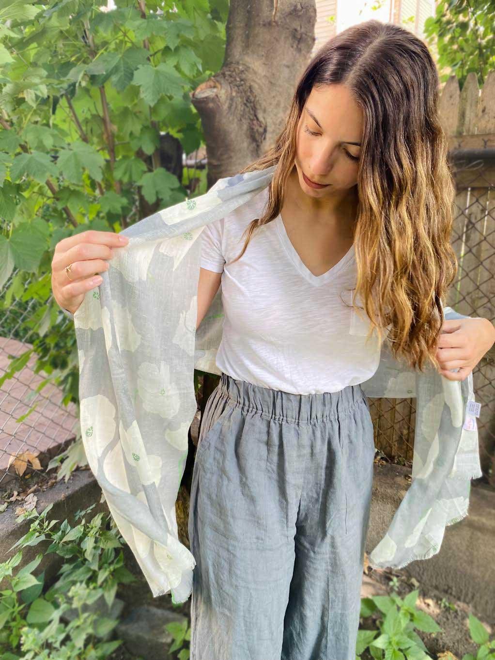 Woman outdoors holding a light floral poppies scarf, wearing white t-shirt and gray pants