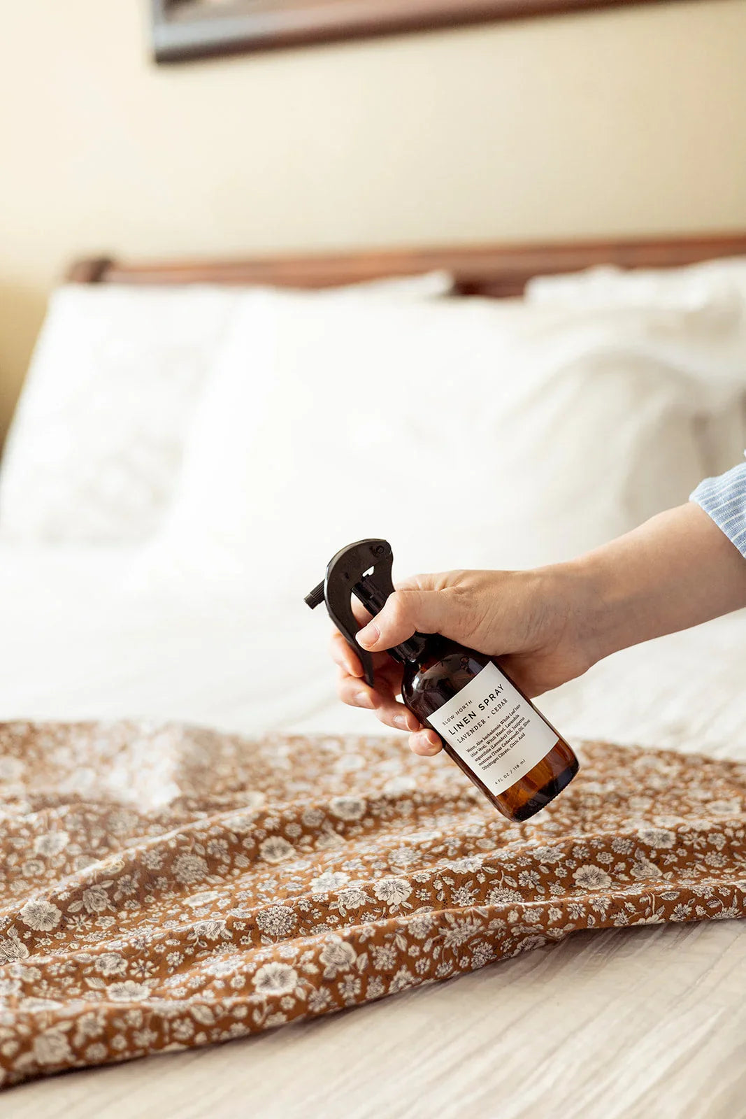 Hand spraying lavender cedar linen spray on floral fabric in cozy bedroom from Qu!rk Boutique.