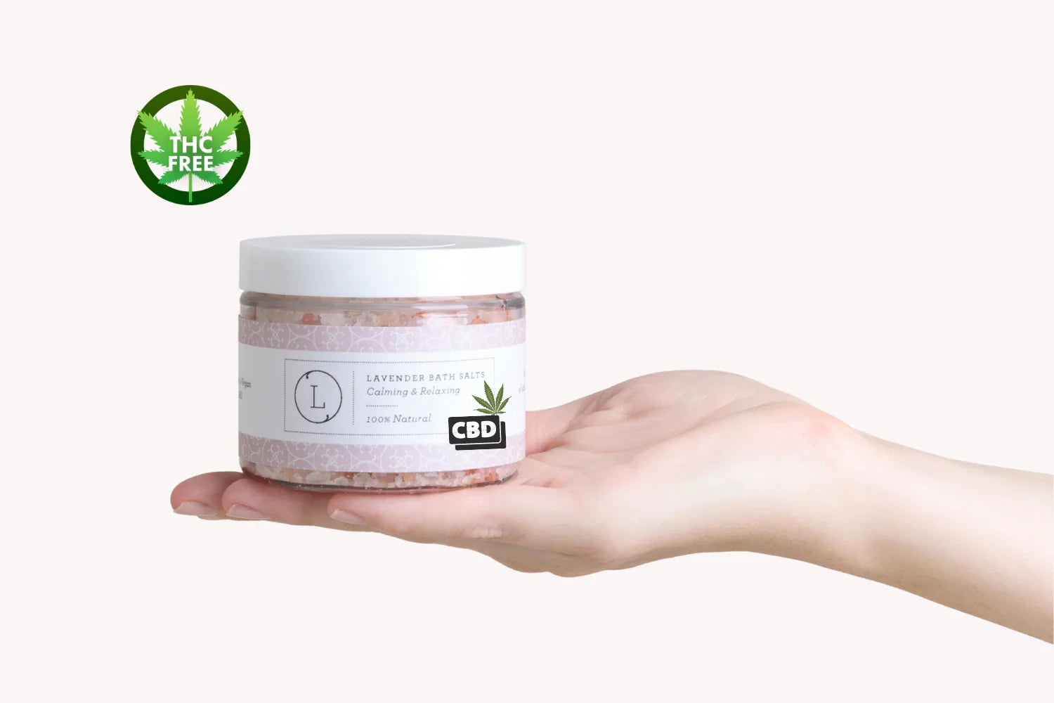 Hand holding jar of lavender CBD bath salts labeled calming, relaxing, 100% natural, THC free