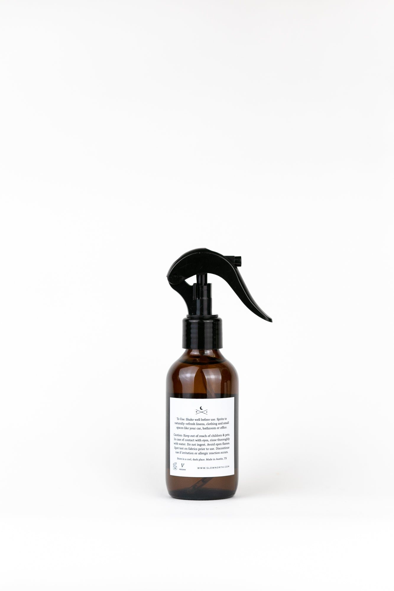 Amber glass spray bottle with black trigger nozzle and white label on white background