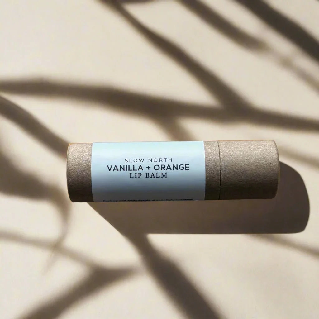 Vanilla and orange scented lip balm tube by Slow North on beige background with shadow