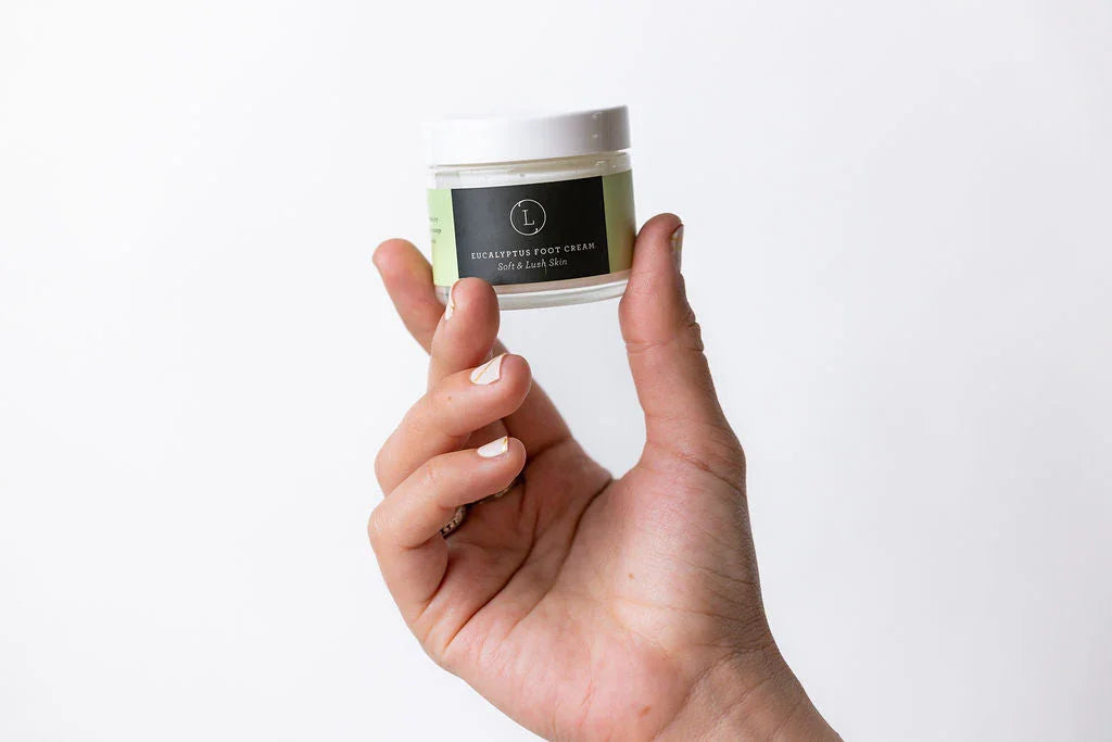 Hand holding a small jar of eucalyptus shea butter foot cream with a minimalist label