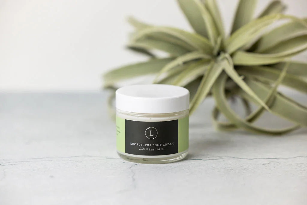 Jar of eucalyptus foot cream with white lid on marble surface, green plant background