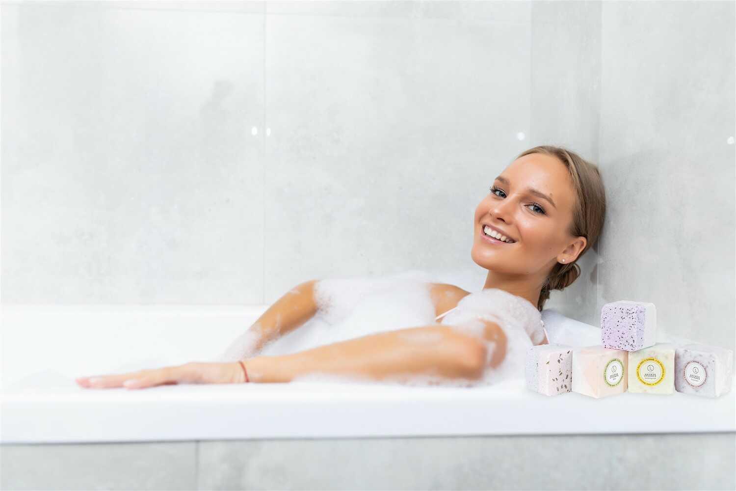 Smiling woman relaxing in a bubble bath with natural shower steamers displayed on tub edge
