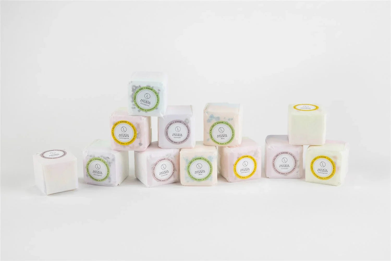 Stacked natural shower steamers in pastel packaging with labels for eucalyptus, lemongrass, lavender, and mint scents