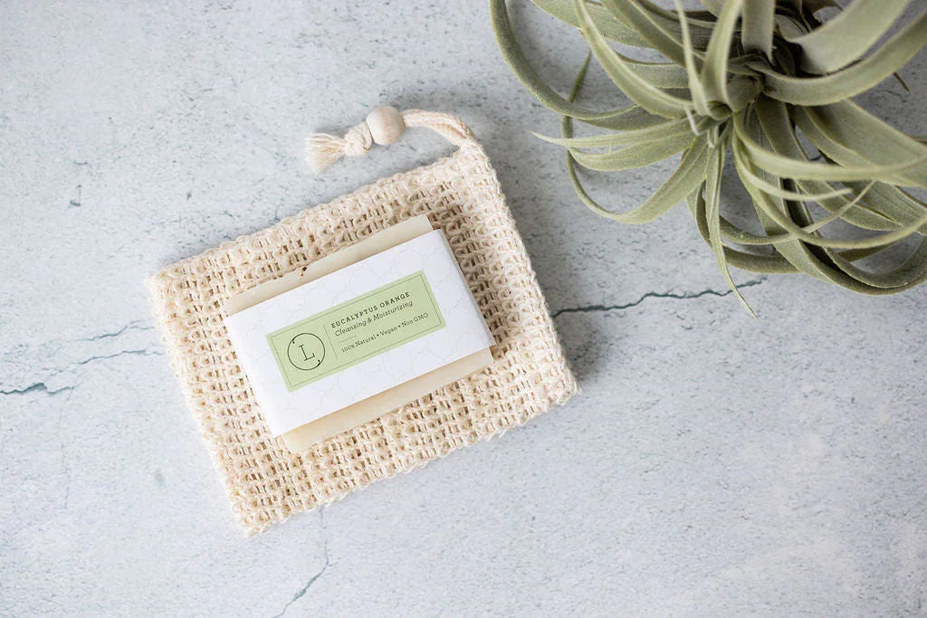Natural eucalyptus orange soap bar on a woven soap pouch beside green air plant on concrete surface