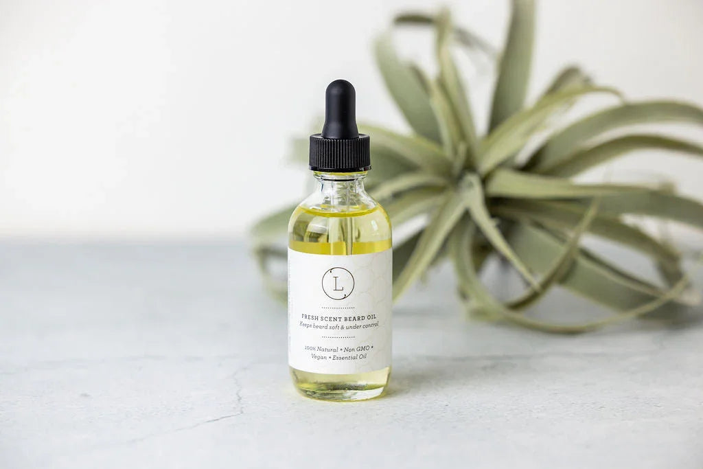 Bottle of natural fresh scent beard oil with dropper on gray surface and green plant