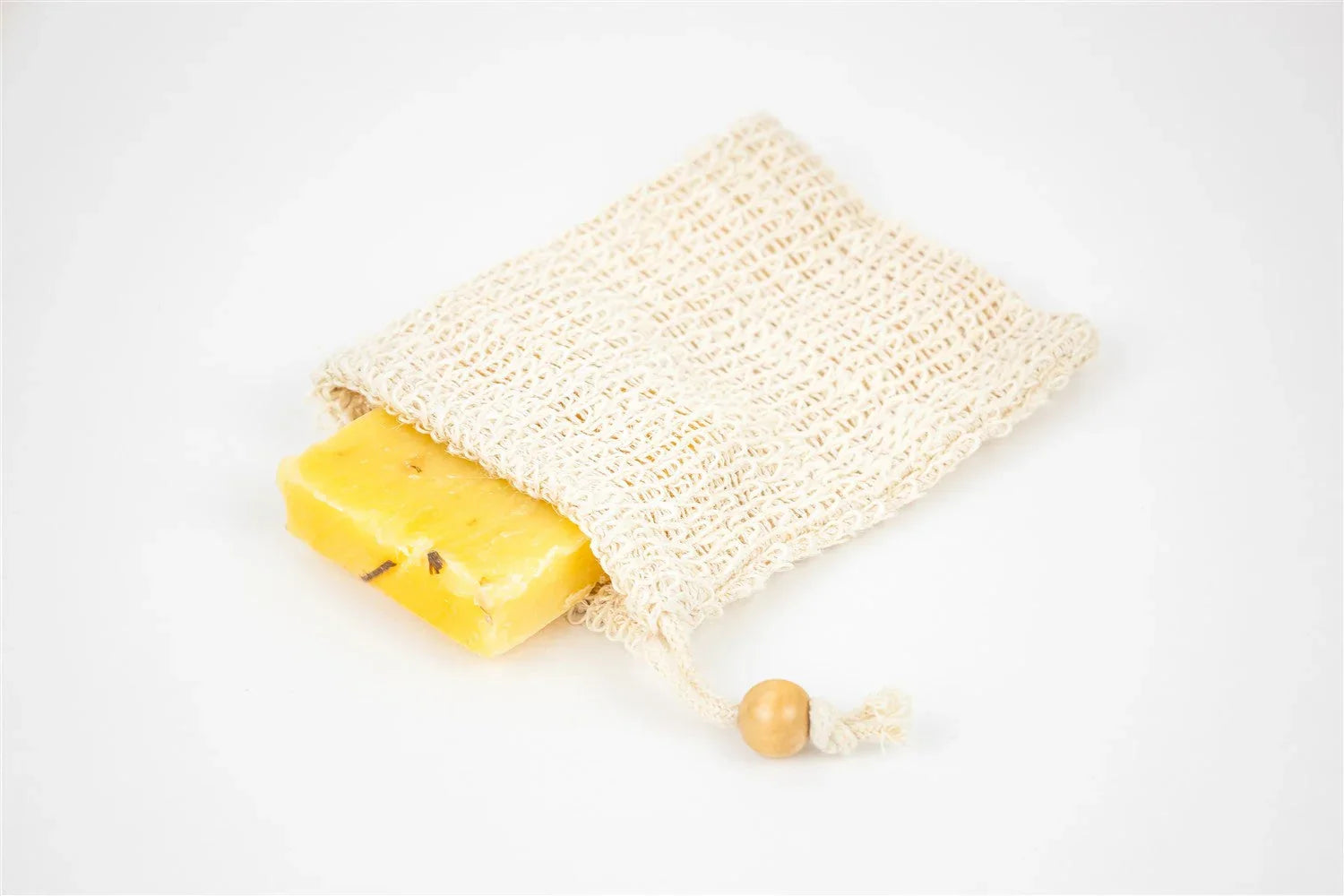 Yellow soap bar partially inside a natural beige luffa soap saver pouch with a wooden bead