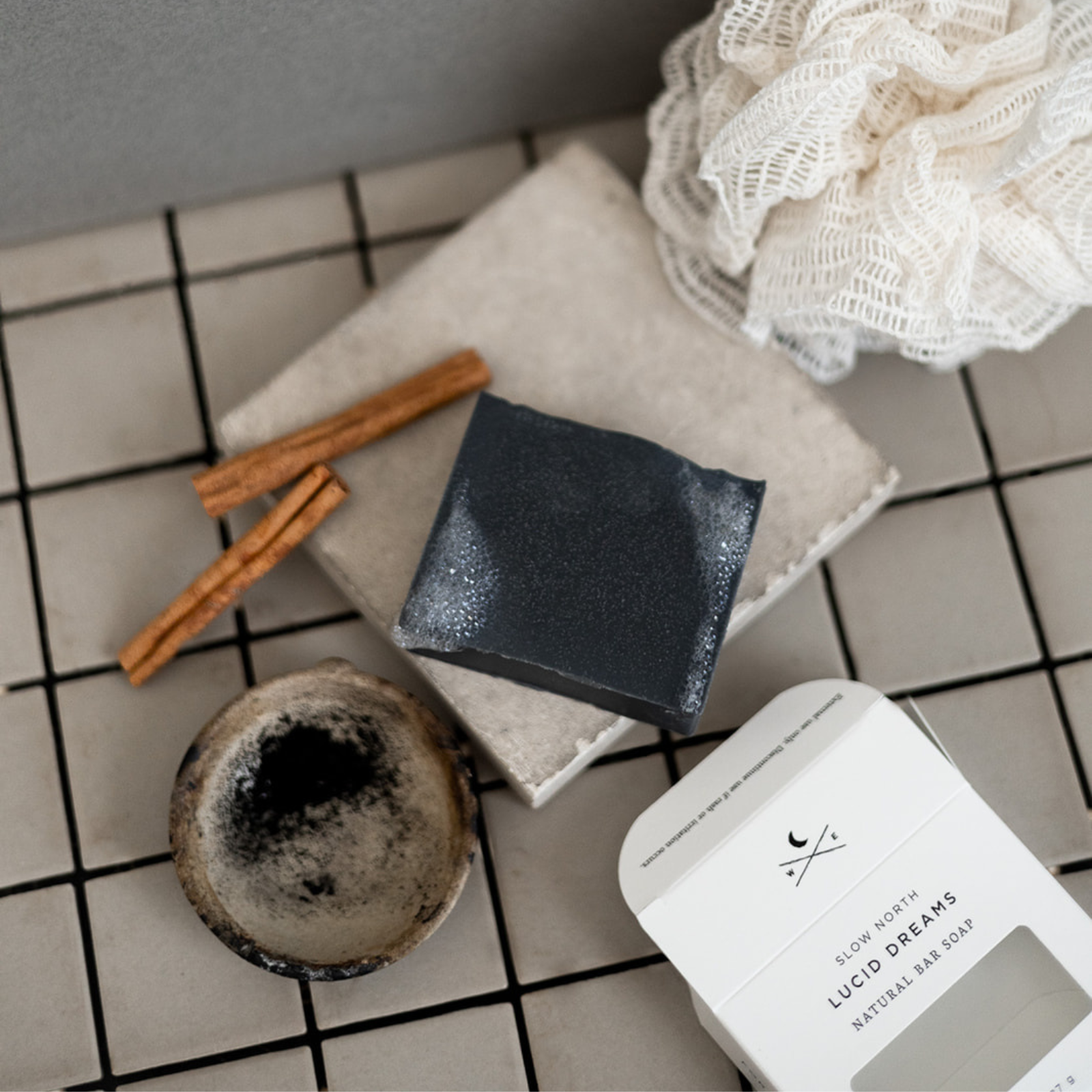 Black bar soap with bubbles on stone tile, Slow North Lucid Dreams natural bar soap packaging
