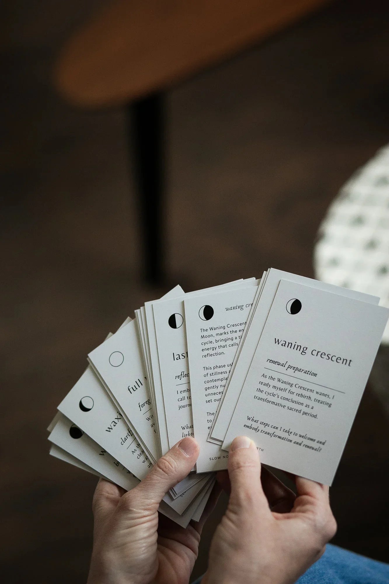 Hands holding moon phase cards including waning crescent with lunar cycle descriptions