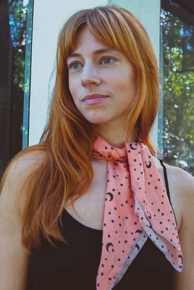 Red-haired woman in black tank top wearing pink scarf with moon and star patterns outdoors