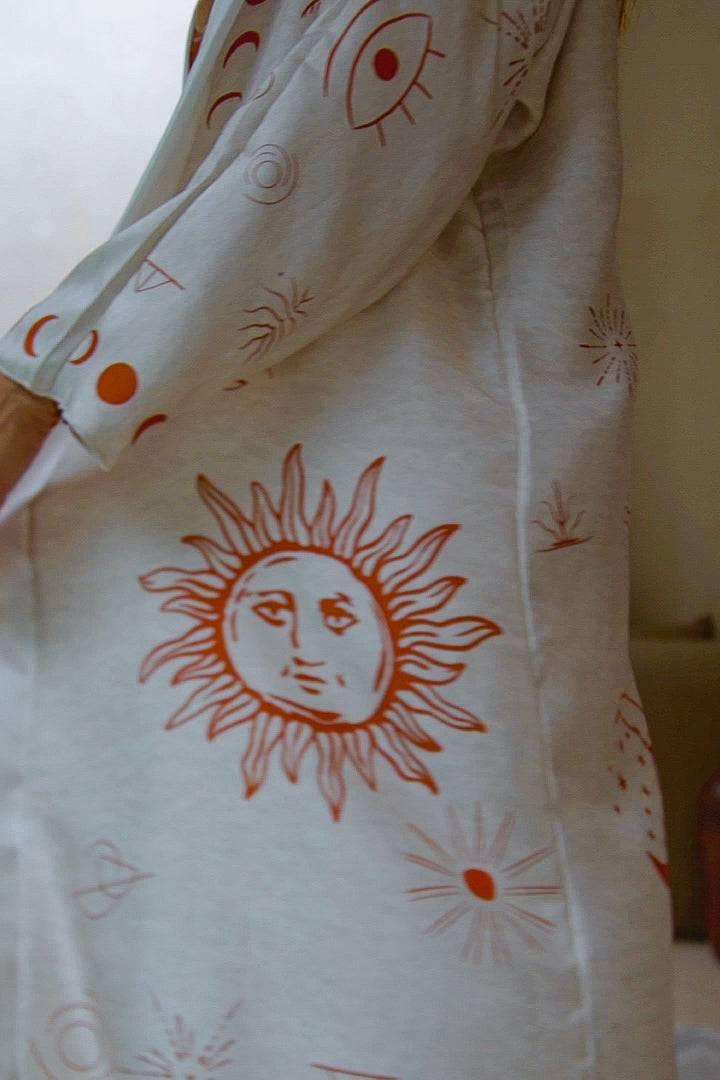 Close-up of beige fabric with orange sun, eye, and moon celestial prints on clothing sleeve and side